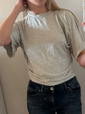 Ljusgrå basic t-shirt - Enkel och stilren ljusgrå t-shirt med rund hals och korta ärmar. Perfekt till jeans eller shorts för en avslappnad look. T-shirten har en loose passform och är tillverkad i mjuk bomull.