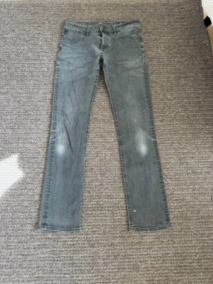Jeans - Passar 32/34. Snygga grå jeans med raka ben och knappgylf. Klassisk femficksmodell med bälteshällor och diskret slitning på låren. Perfekta för en avslappnad och trendig look.