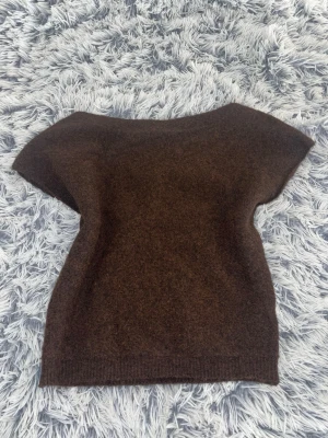 Mörkbrun stickad topp - Säljer en enkel och stilren mörkbrun stickad topp med korta ärmar och rund hals. Toppen har en mjuk och lite luddig yta, perfekt för lager på lager eller som den är. Passar dig som gillar minimalistisk och klassisk stil.