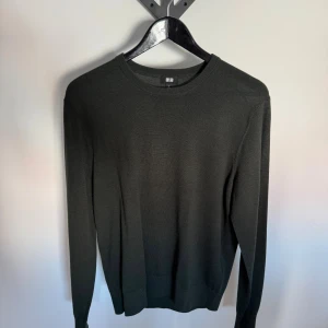 Mörkgrön stickad tröja från Uniqlo - En stilren mörkgrön stickad tröja från Uniqlo med rund halsringning och långa ärmar. Tröjan har en smal passform och ribbade muddar vid ärmslut och nederkant. Perfekt för lager-på-lager och enkel att matcha med olika outfits.