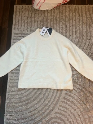 Vit stickad tröja med rund hals - Klassisk vit stickad tröja med rund hals och långa ärmar. Tröjan har ribbade muddar vid ärmslut och nederkant för en clean look. Perfekt att matcha med jeans eller kjol för en enkel och stilren outfit. Den är aldrig använd och har prislappen kvar. Säljer då den inte längre går att skicka tillbaka. 💕