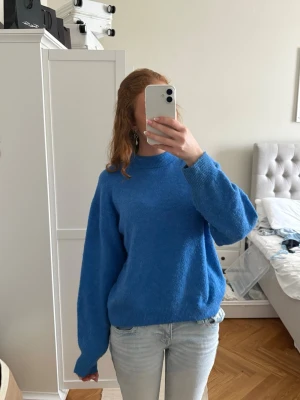 Blå stickad tröja med rund hals - Mysig blå stickad tröja med rund hals och långa ärmar. Tröjan har ribbstickade muddar vid ärmslut och nederkant. Perfekt för lager-på-lager och enkel att styla till jeans eller kjol.
