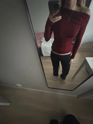 Mörkröd offshoulder topp - Snygg mörkröd offshoulder topp med lång ärm och tight passform. Toppen har en stilren design och är lätt att matcha med olika outfits. Perfekt för dig som gillar trendiga och bekväma plagg.