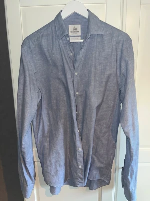 Blå skjorta från The Shirt Factory - Blå linneskjorta från The Shirt Factory i Regular fit, storlek 38 med extra lång ärm. Nyskick. Säljs på grund av för stor storlek.