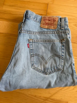 Levi's 517 ljusblå jeans - Klassiska ljusblå Levi's 517 jeans med rak passform och hög midja. Jeansen har den ikoniska röda Levi's-lappen på bakfickan och patch i läder bak i midjan. Tillverkade i slitstark denim, perfekta för en avslappnad och tidlös stil.