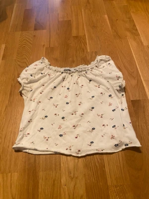 Vit blommig blus med kort ärm - Söt vit blus med små blommor i blått och rosa. Blusen har korta ärmar med volangkant, elastisk halsringning som kan bäras offshoulder. Perfekt för sommarens alla dagar. Blev dock inte jättebra bilder…
