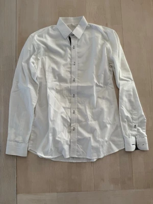 Klassisk vit skjorta med knappar - Stilren vit skjorta med lång ärm och knappar framtill. Skjortan har klassisk krage och är tillverkad i ett mjukt bomullstyg som passar perfekt till många olika looks.