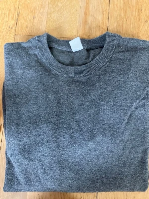 Mörkgrå stickad tröja från Lindex - En enkel och stilren mörkgrå stickad tröja från Lindex. Tröjan har rund halsringning och är tillverkad i mjukt material som passar perfekt till vardags. Passar ungdomar i storlek 158/164.