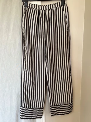 Randiga byxor från Gina Tricot XS - Säljer ett par svartvita byxor från Gina Tricot i storlek XS. Byxorna har vertikala ränder, raka ben och resår i midjan. Tillverkade i ett mjukt, lätt silkesmaterial. Perfekta för en trendig och avslappnad look.