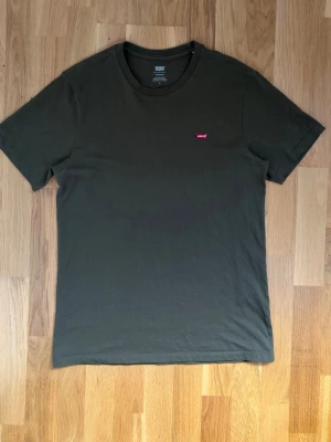 Mörkgrön t-shirt från Levi's - Snygg mörkgrön t-shirt från Levi's med klassisk passform och rund hals. Diskret Levi's-logga i rött på bröstet. Tillverkad i mjuk bomull som känns skön mot huden. Perfekt basplagg för en enkel och stilren look.