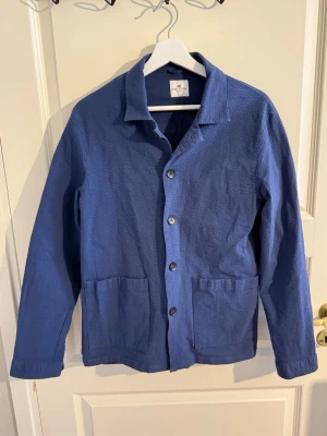 Blå overshirt från John Henric - Säljer en blå overshirt från John Henric i storlek M. Skjortjackan har en avslappnad passform, två stora framfickor och stängs med fyra knappar. Materialet är strukturerat bomullstyg som ger en schysst känsla och look. 