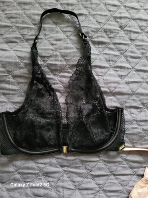 Svart spets-bh - Snygg svart bh i genomskinlig spets med triangelformade kupor och dekorativa gulddetaljer. Bh:n har justerbara axelband och knäppe fram. Materialet är mjuk spets och mesh som ger en elegant look.