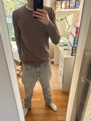 Brun rundhalsad tröja - En enkel och stilren brun tröja med rund halsringning och långa ärmar. Tröjan har ribbade muddar vid ärmslut och nederkant, vilket ger en snygg passform. Perfekt att matcha med jeans för en avslappnad look.