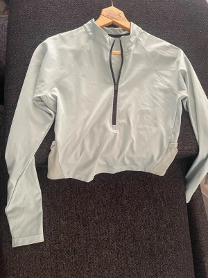 Ljusgrön cropped träningströja - Ljusgrön långärmad sporttröja med halv dragkedja framtill och hög krage. Tröjan har en smal passform och en diskret ficka med dragkedja på ryggen.. Tillverkad i ett stretchigt funktionsmaterial.