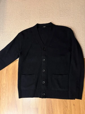 Marinblå stickad kofta/cardigan - Stickad mörkblå ull kofta/cardigan med knappar framtill. Två fickor framtill och ribbade muddar vid ärmslut och nederkant. Perfekt att slänga över en t-shirt för en clean look. Tröjan är köpt på en Uniqlo butik i Japan på en resa. Den är knappt använd i mycket bra skick. 