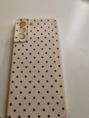 Beige mobilskal med svarta prickar - Snyggt beige mobilskal med svarta prickar i ett prickigt mönster. Skalets material känns mjukt och flexibelt, troligen silikon eller TPU. Passar en mobil med tre kameralinser och en blixt. Perfekt för dig som vill ha ett unikt och trendigt skal. Är från fyndiq och är i storleken samsung s21 5g. Alldrig använd då jag råkade köpa fel storlek !