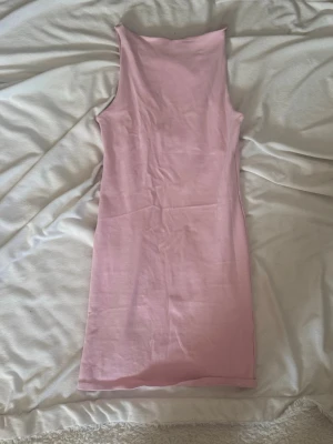 Rosa ärmlös kortklänning - Säljer en enkel och stilren rosa kortklänning i mjukt material. Klänningen är ärmlös och har en rak passform som ger en clean look. Perfekt för varma dagar eller att styla med accessoarer.ribbat material