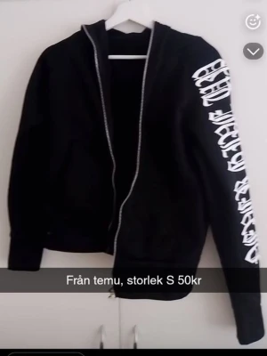 Svart hoodie med vit text på ärmen - Cool svart hoodie från Temu med dragkedja och stor vit text i grafisk stil längs ena ärmen. Klassisk huva och ribbade muddar vid ärmslut och nederkant. Perfekt för en streetwear-look och enkel att matcha med jeans eller joggers.