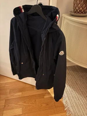Moncler windbraker - En mörkblå windbrkaer från moncler, perfekt nu till våren. Metallbiten på ena snöret är borta (se bild tre). Inget kvitto eller påse eller något där av priset. Kan garantera att den är äkta.