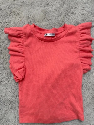 Rosa topp med volangärmar från Zara - Supersöt rosa topp från Zara med ribbad struktur och volangdetaljer på ärmarna. Modellen är kortare och har rund halsringning. Perfekt för dig som vill ha något färgglatt och trendigt i garderoben.
