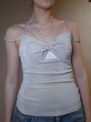 Ljusbeige omlott linnetopp - Trendig ljusbeige linnetopp med flera tunna axelband och omlottdetalj framtill. Toppen har en twistad knut vid bysten och en liten trekantig öppning. Sitter tight och är perfekt till jeans eller kjol.