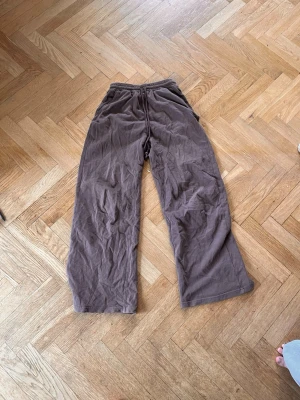 Bruna vida mjukisbyxor - Säljer ett par bruna mjukisbyxor med bred passform och resår i midjan. Byxorna har dragsko för justerbar midja och är tillverkade i ett mjukt, bekvämt material. Perfekta för chill dagar hemma eller när du vill ha det extra bekvämt. Skriv gärna för mått! 💝