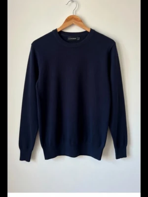 Marinblå stickad tröja J.Lindeberg storlek S - Snygg marinblå stickad tröja från J.Lindeberg i storlek S. Tröjan har rund hals och långa ärmar, perfekt för dig som gillar stilrena och klassiska plagg. Materialet är mjukt och skönt, passar bra till både jeans och chinos.