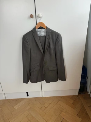 Kostym från Tiger of Sweden  - Snygg grå/grön kostym med klassisk kavaj och matchande byxor. Kavajen har två knappar, fickor med lock och smal passform. Perfekt för dig som vill ha en stilren och tidlös look. Passar till många olika tillfällen. Nypris 5490 kr 