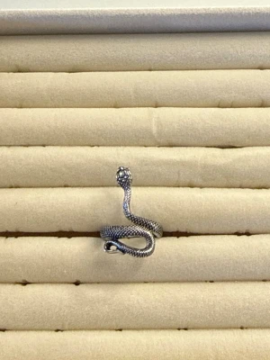 Silvrig orm ring  - Cool ring i form av en slingrande orm, tillverkad i silvrig metall med detaljerad yta som liknar ormskinn. Ringen är öppen och justerbar, vilket gör att den passar de flesta fingrar. Perfekt accessoar för dig som gillar unika och edgy smycken.