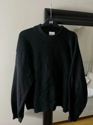 Svart stickad tröja från H&M - En enkel och stilren svart stickad tröja från H&M. Tröjan har rund halsringning, långa ärmar och en avslappnad passform. Perfekt att matcha med jeans eller kjol för en clean look. Materialet känns mjukt och bekvämt mot huden.