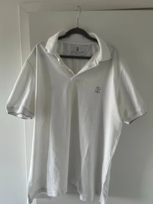 Vit piké från Brunello Cucinelli - Klassisk vit pikétröja från Brunello Cucinelli med kort ärm och diskret logga broderad på bröstet. Tillverkad i mjuk bomull och har en stilren krage med knappslå. Ny pris 550 £