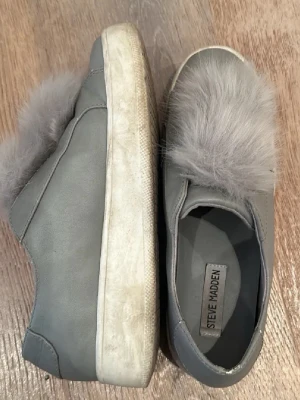 Grå sneakers med fuskpäls Steve Madden - SÅ SNYGGA sneakers från Steve Madden med fluffig fuskpälsdetalj på ovansidan och tjock vit platåsula. Skorna är i mockaimitation och har en slip-on design utan snörning. 
