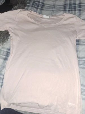 Ljusrosa ribbad t-shirt - En enkel och stilren ljusrosa t-shirt med rund halsringning och korta ärmar. T-shirten har en ribbad struktur som ger en snygg detalj och är tillverkad i mjuk bomull för skön komfort. Perfekt basplagg till garderoben.