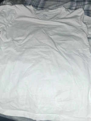 Vit basic t-shirt från 157 - En klassisk vit t-shirt från 157 med rund hals och korta ärmar. Tillverkad i mjuk bomull som känns skön mot huden. Perfekt att matcha med jeans eller shorts för en enkel och clean look.