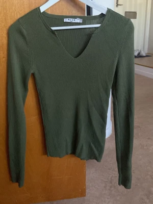 Olivgrön ribbstickad tröja NA-KD - olivgrön ribbstickad tröja från NA-KD med v-ringning och långa ärmar. Aldrig använd. Provat en gång.