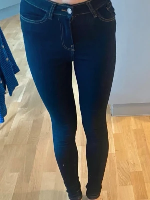Mörkblå skinny jeans från Happy Holly - Säljer ett par mörkblå skinny jeans från Happy Holly  med hög midja och klassiska fem fickor. Jeansen har stretchigt material och kontrastsömmar som ger en snygg siluett. Perfekta till sneakers eller boots!