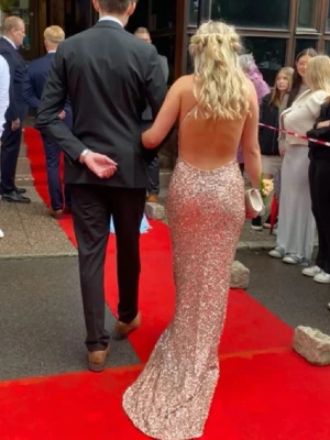 Glittrig långklänning med öppen rygg - Nypris 5000kr, kollq sista bild. Säljer en superglittrig långklänning i champagnefärg med öppen rygg och figurnära passform. Klänningen har tunna axelband och är helt täckt av paljetter som fångar ljuset. Perfekt för bal eller festkvällar när du vill sticka ut.