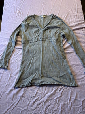 Ljusgrön ribbad långärmad topp - Säljer en ljusgrön ribbad topp med v-ringning och långa ärmar. Toppen har fina spetsdetaljer runt halsen och under bysten, vilket ger en feminin touch. Perfekt att styla med jeans eller kjol för en trendig look.