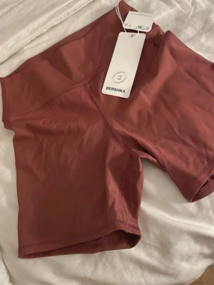 Rostbruna cykelshorts från Bershka - Snygga rostbruna cykelshorts från Bershka med hög midja och tight passform. Tillverkade i ett stretchigt syntetmaterial som passar perfekt till träning eller en sportig look. Stilrena utan mönster eller extra detaljer.