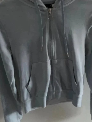 Blå mjukis tröja  - En stilren blå hoodie med dragkedja framtill och två stora fickor. Tröjan har huva med dragsko och ribbade muddar vid ärmslut och nederkant. Perfekt för en avslappnad look och enkel att matcha med andra plagg.