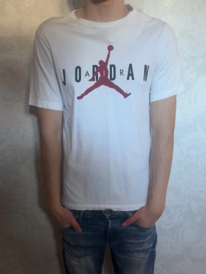 Vit Jordan t-shirt med logga - Säljer en vit t-shirt från Jordan med den klassiska Jumpman-loggan i rött och svart text på bröstet. T-shirtens krage runt halsen är lite konstig då jag haft den länge som ni kan se på sista bilden annars inga fel med den. Priset är inte hugget i sten.