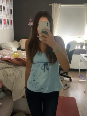 Ljusblå linnetopp med blommönster - Säljer en ljusblå linnetopp med blommönster och knytband under bysten. Toppen är ärmlös och har en avslappnad passform, perfekt för varma dagar. Detaljerna med knyt och blommor ger en söt och fräsch look.