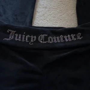 Svarta velourbyxor Juicy Couture - Mysiga svarta velourbyxor från Juicy Couture med loggan i glittrande stenar på baksidan. Perfekta för chill dagar hemma eller när du vill ha en avslappnad men ändå snygg look. Klassisk modell med mjukt material och bekväm passform.