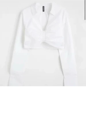 Vit croppad blus med twist - Trendig vit croppad blus med lång ärm och krage. Toppen har en snygg scrunch-detalj framtill och djup v-ringning. Perfekt att styla   för en cool look. Endast testad men för liten för mig