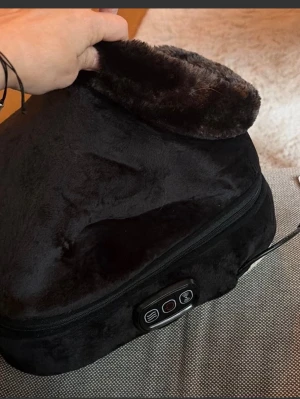 Svart elektrisk fotvärmare - Mysig svart elektrisk fotvärmare i mjukt, fluffigt material. Har en öppning för fötterna och en kontrollpanel med knappar för värmeinställning. Perfekt för kalla dagar när du vill värma fötterna snabbt och enkelt.