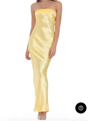 Elegant gul satinklänning från Lucy in the Sky - Gul satinklänning från Lucy in the Sky Elegant, axelbandslös maxiklänning i glansigt satin med figurnära passform och knytning i rygg. Perfekt till fest eller bal Helt ny – aldrig använd, fortfarande i originalförpackning. 