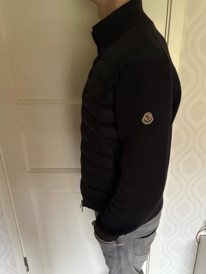 Mörkblå cardigan  från Moncler - Snygg mörkblå cardigan från Moncler med quiltad framsida och Moncler-logga på ärmen. Jackan har hög krage, dragkedja framtill och ribbade muddar. Perfekt för dig som vill ha en stilren och modern look.