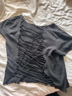 Svart t-shirt med slitsad framsida - Cool svart t-shirt med korta ärmar och unik slitsad design framtill. T-shirten har en lös passform och är tillverkad i mjuk bomull. Perfekt för dig som vill sticka ut med en edgy och trendig stil.