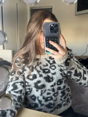 Beige leopardmönstrad stickad tröja - Säljer en stickad tröja i grått med svart leopardmönster. Tröjan har rund halsringning och ribbade muddar vid ärmslut och nederkant. Perfekt för dig som vill ha en trendig och mysig look till hösten eller vintern.