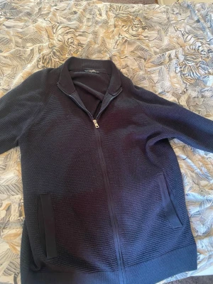 Mörkblå ziptröja med krage - Säljer en mörkblå ziptröja med krage och två fickor framtill. Tröjan har en diskret struktur i materialet och dragkedja hela vägen. Perfekt för lager på lager och enkel att matcha med olika outfits.
